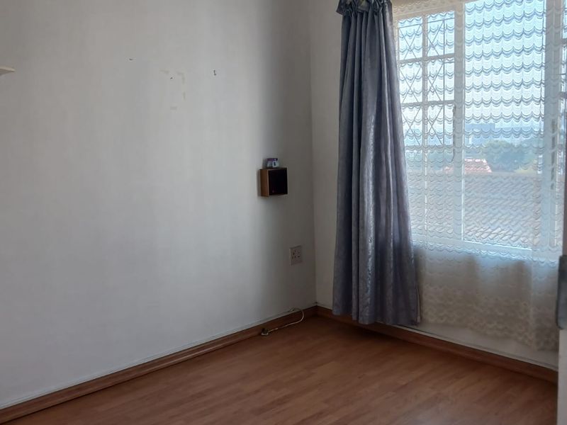 An empty bedroom featuring laminate flooring, a window with security bars, and a ventilation grille. The room requires minor wall repairs and cosmetic updates.