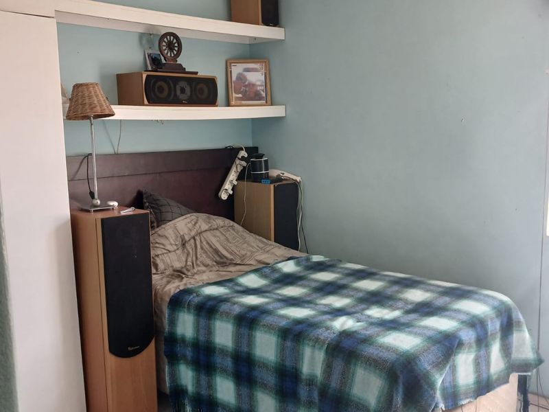 A compact bedroom featuring tiled flooring, a ceiling fan, and built-in wardrobe storage with floating shelving.