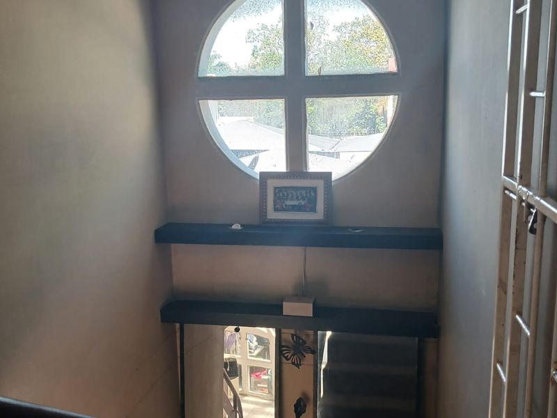 A staircase landing area featuring a distinctive circular window, built-in shelving, and a metal security gate.