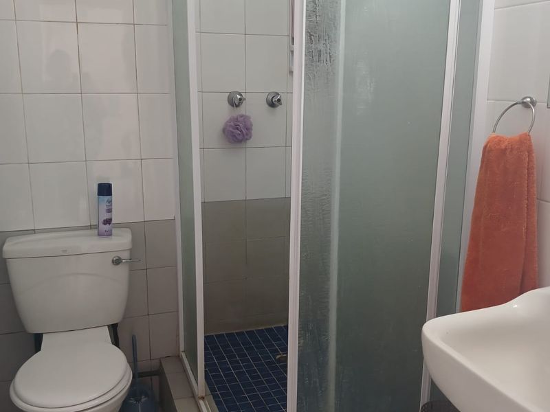 A functional bathroom featuring a shower enclosure, pedestal basin, and toilet with white wall tiling and blue mosaic shower floor tiles.