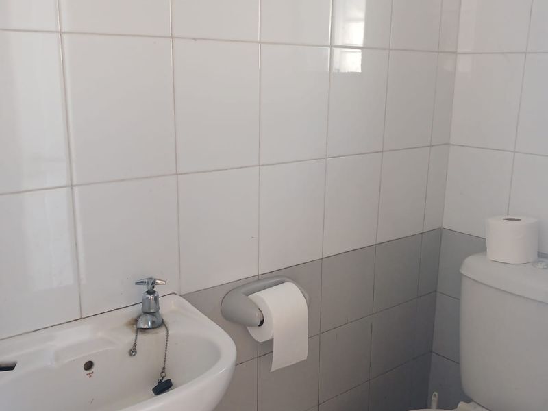 A compact bathroom featuring a wall-mounted basin and standard toilet with white and grey wall tiling.