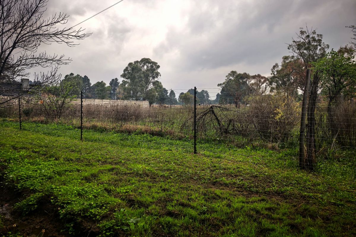 A view of a vacant residential plot featuring overgrown grass, natural vegetation, and perimeter wire fencing under an overcast sky.