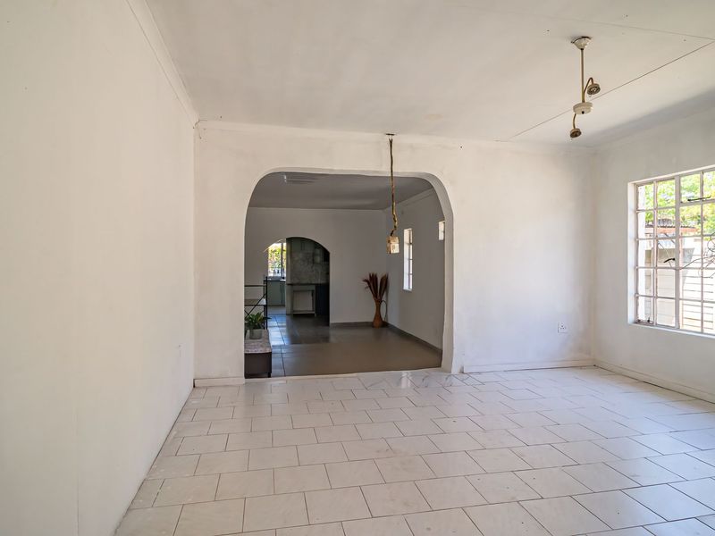 An empty open-plan living area featuring tiled flooring, an arched transition to the kitchen, and large steel-framed windows allowing natural light.
