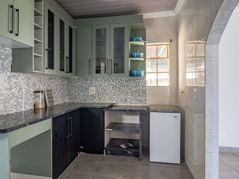 A functional kitchen featuring sage green and black cabinetry, mosaic tile backsplash, stone-look countertops, and ceramic floor tiling.