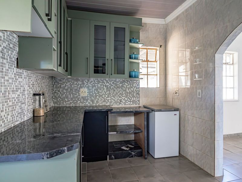 A functional kitchen featuring sage green cabinetry, stone countertops, mosaic tile backsplash, and ceramic wall and floor tiling.