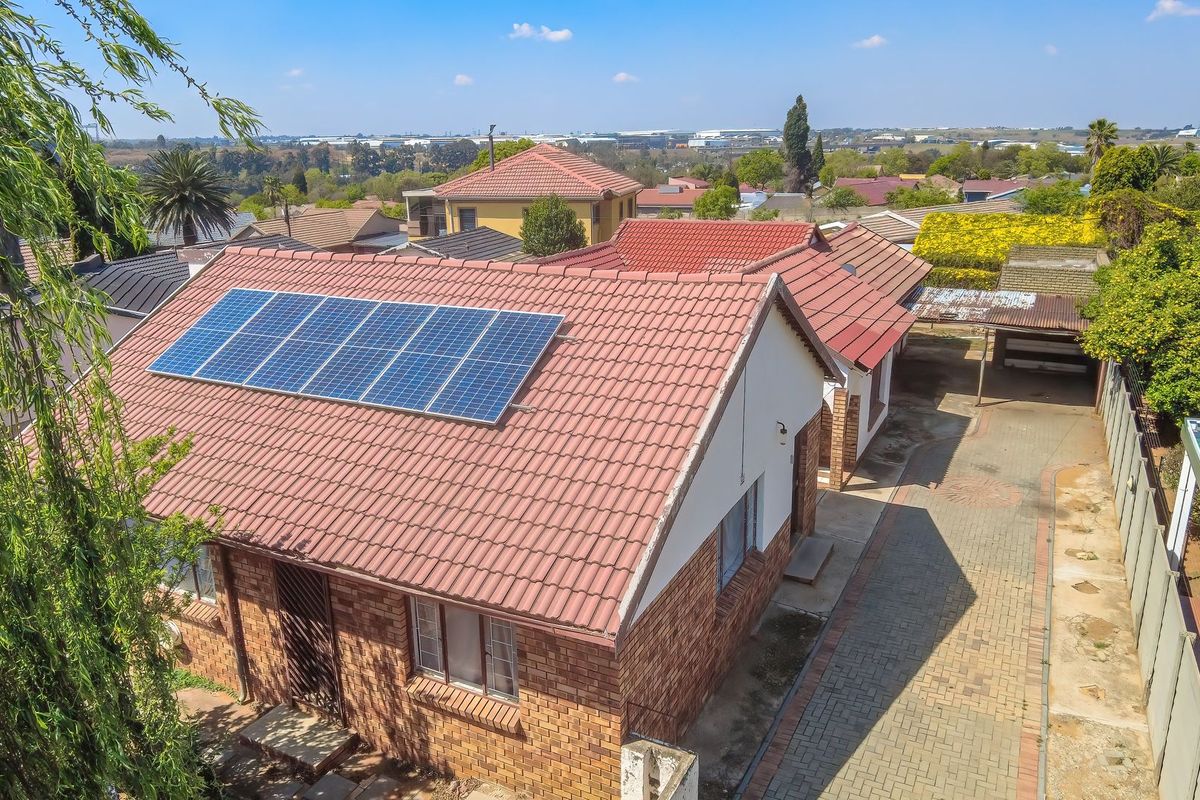 Aerial view of a residential property featuring a brick exterior, tiled roof with installed solar panels, and a paved driveway with a carport.