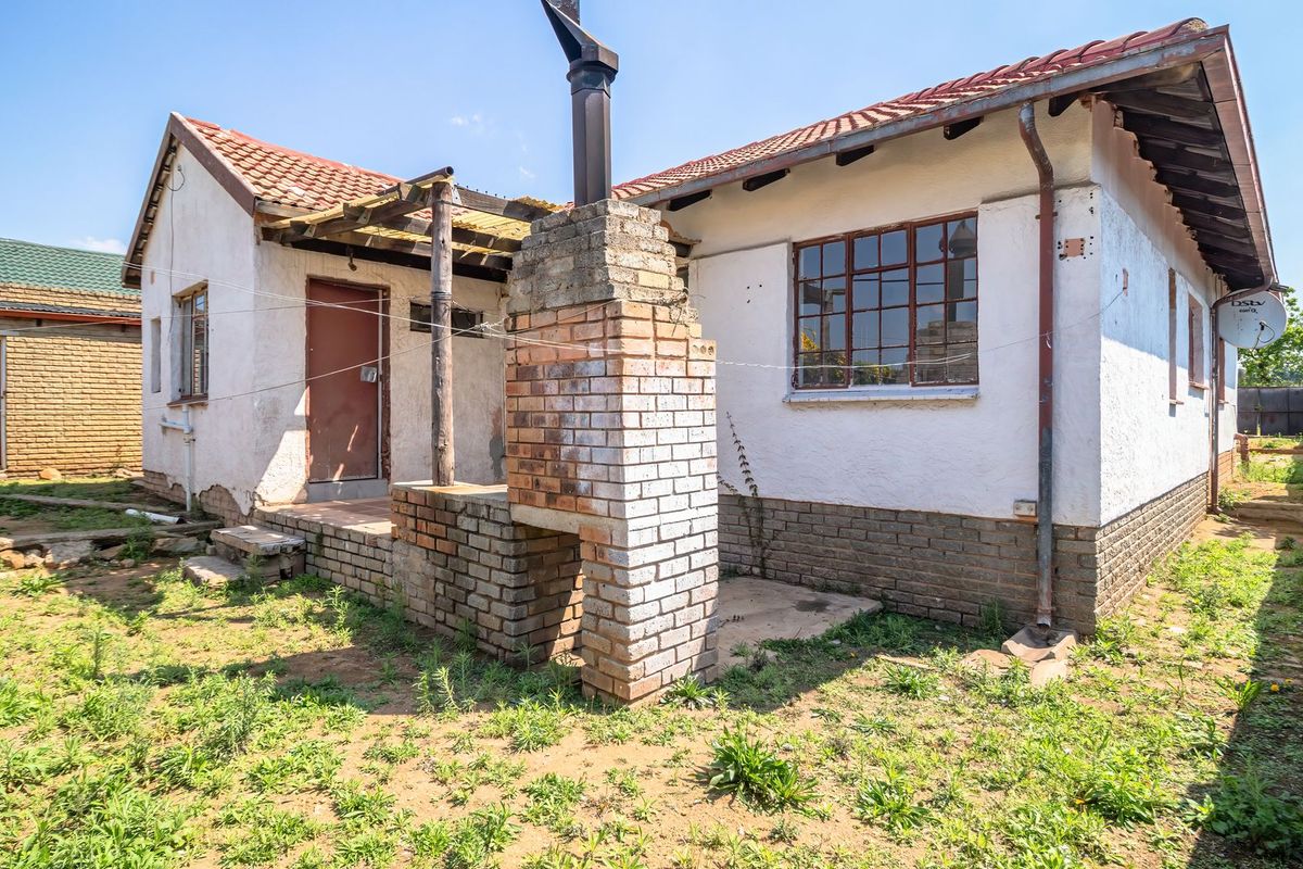 Rear view of the property featuring a brick chimney, tiled roof, and steel window frames, set against a large backyard area.