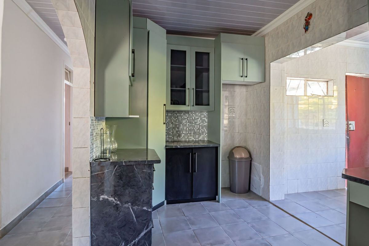 A functional kitchen space featuring built-in cabinetry, stone countertops, and tiled finishes, offering a clean canvas for potential modern updates.