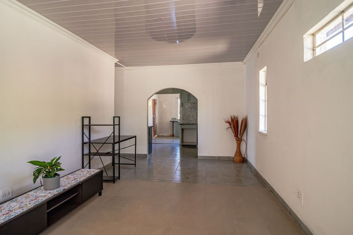A spacious, neutral living area featuring tiled floors, a glossy ceiling, and an arched entryway leading to the kitchen area.