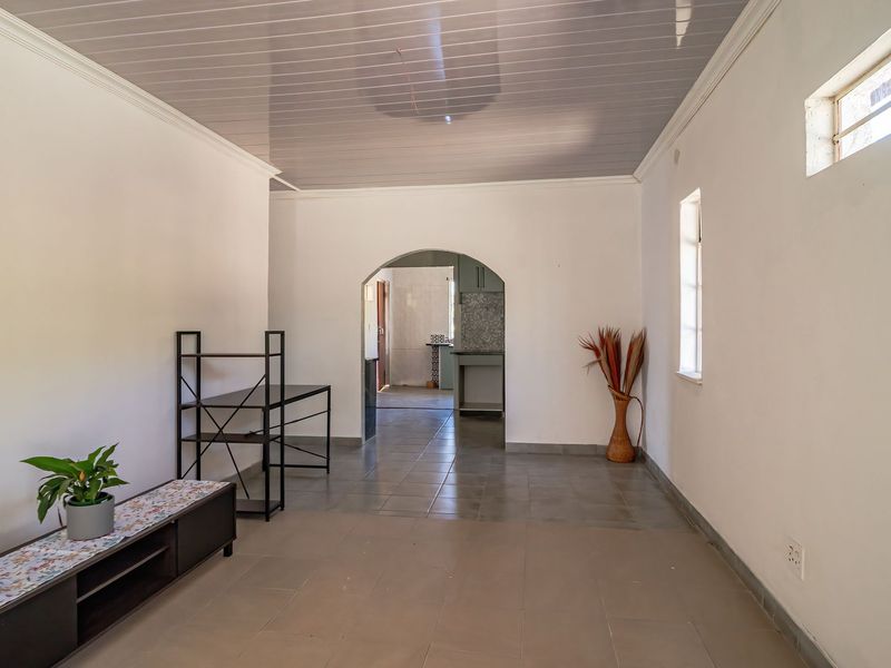 A spacious, neutral living area featuring tiled floors, a glossy ceiling, and an arched entryway leading to the kitchen area.