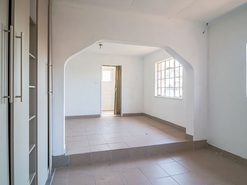 An empty bedroom featuring tiled flooring, built-in cupboards, and a distinct architectural archway leading to an adjoining space.