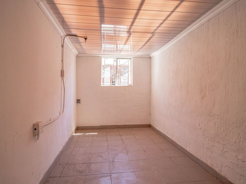 An empty utility space featuring tiled flooring, a window with security bars, and exposed electrical conduit along the wall.