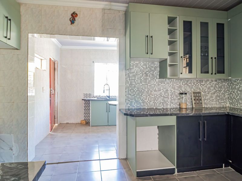 A functional kitchen featuring two-tone cabinetry, mosaic tile backsplashes, and stone countertops, with an adjacent scullery area visible through the doorway.