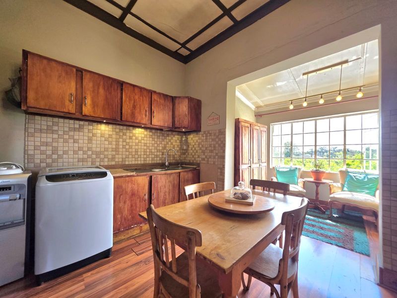 Open plan kitchen and dining area featuring wooden cabinetry, tiled backsplash, and large windows providing natural light and garden views.