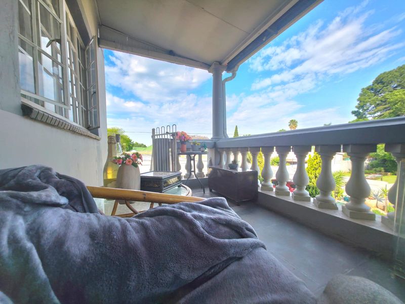 A covered balcony featuring a classic balustrade, tiled flooring, and a support column, offering an outdoor space with potential for cosmetic updates.