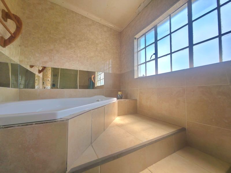 A dated bathroom featuring a built-in bathtub, tiled surfaces, and a large steel-framed window, offering a functional space ready for modernization.