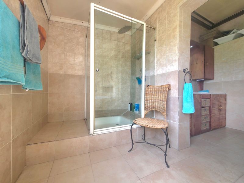 A functional bathroom featuring a glass-enclosed shower, tiled surfaces, and a built-in vanity unit with storage.