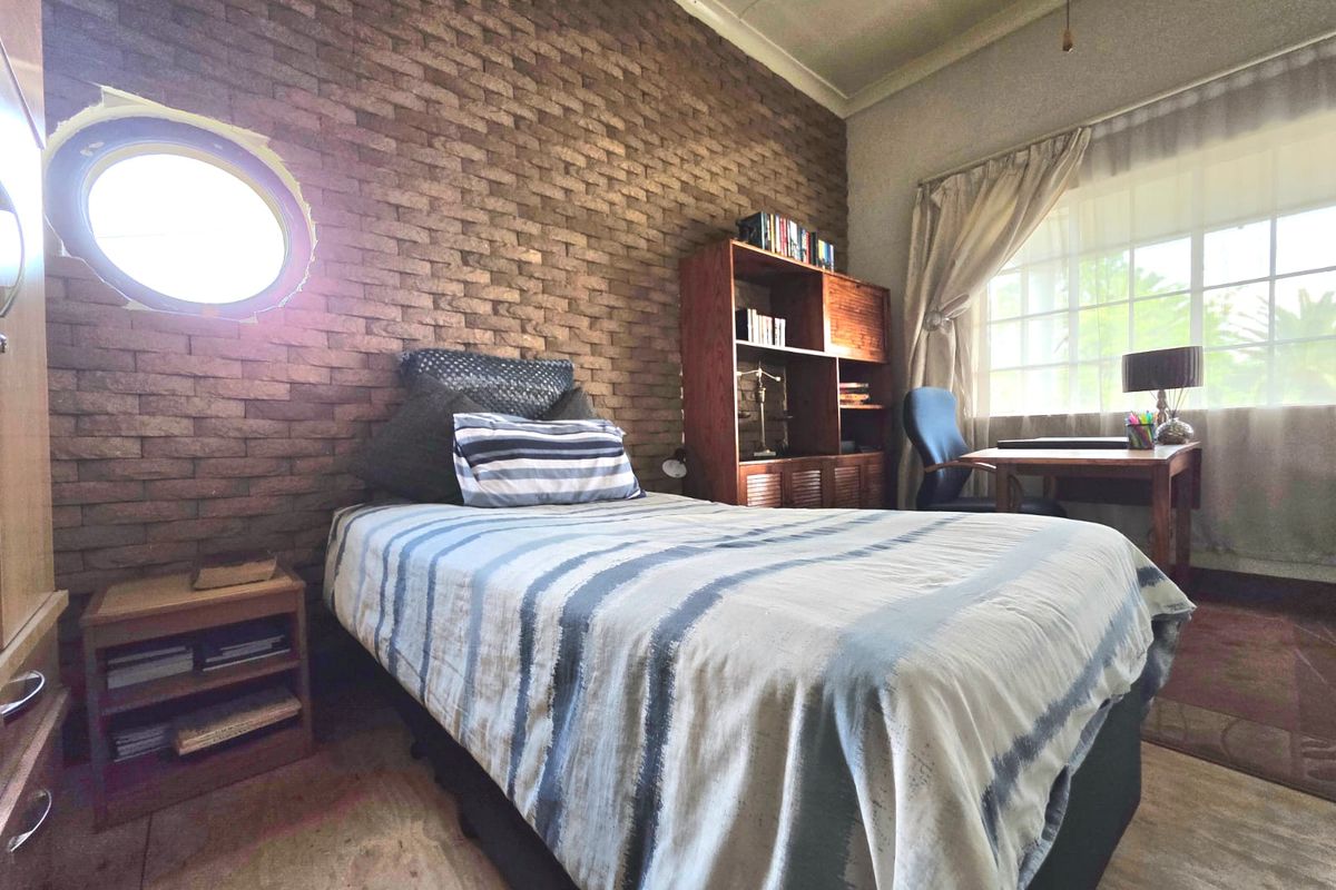 Bedroom featuring an exposed brick feature wall, a unique porthole window, and a large window allowing natural light.