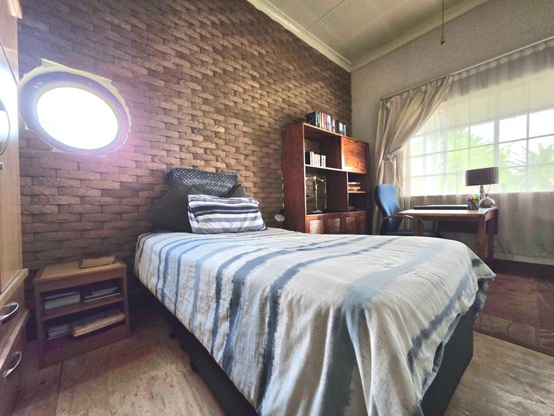 Bedroom featuring an exposed brick feature wall, a unique porthole window, and a large window allowing natural light.