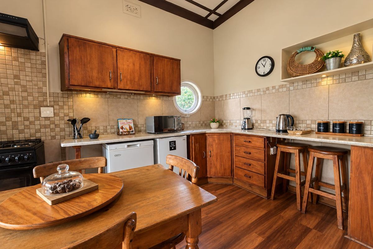 A rustic-style kitchen featuring wooden cabinetry, tiled backsplash, laminate countertops, and a unique porthole window, providing a warm and functional cooking space.