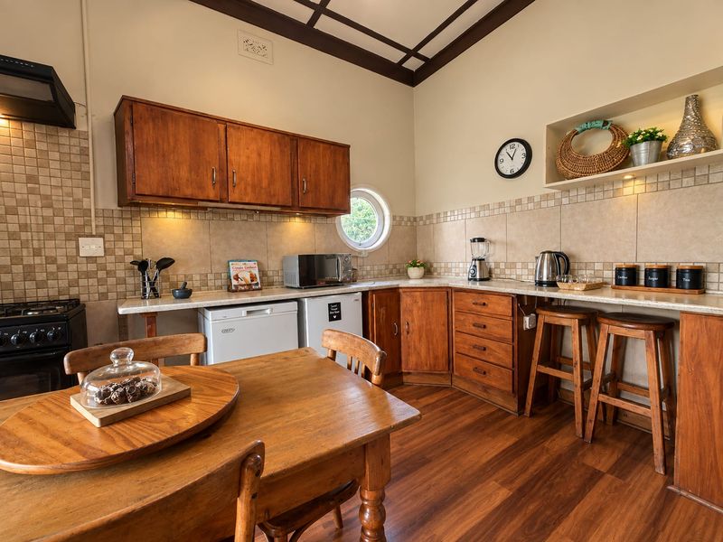 A rustic-style kitchen featuring wooden cabinetry, tiled backsplash, laminate countertops, and a unique porthole window, providing a warm and functional cooking space.