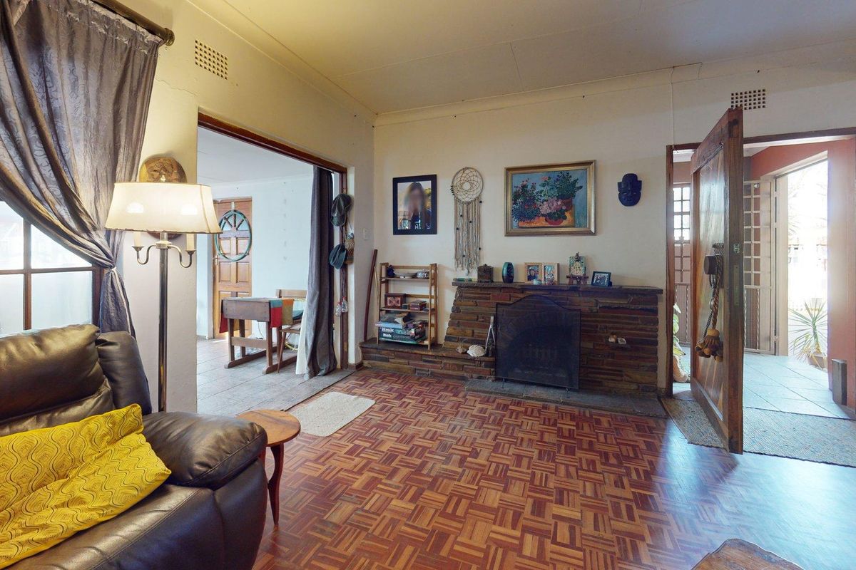 A living room featuring a traditional brick fireplace and classic parquet flooring, with direct access to adjacent rooms through timber-framed doorways.