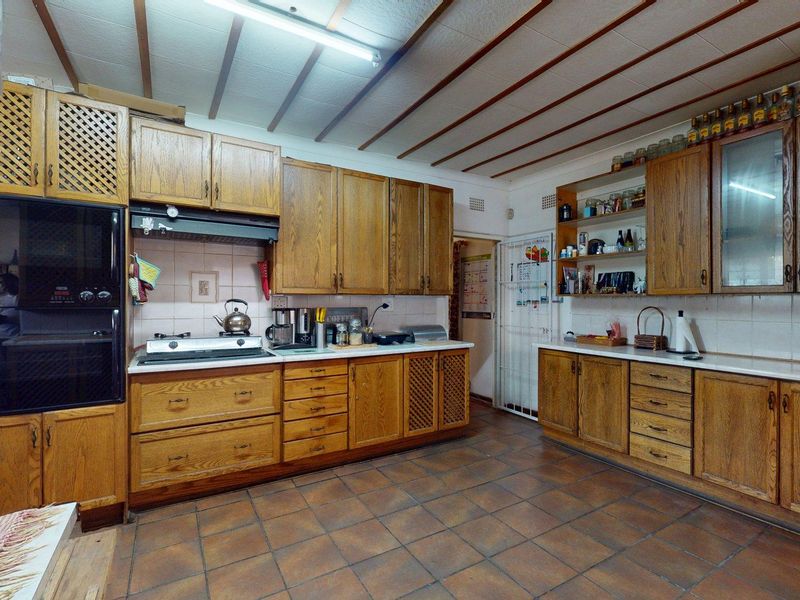 A spacious, dated kitchen featuring extensive wooden cabinetry, tiled flooring, and built-in appliances, offering significant potential for a modern renovation.