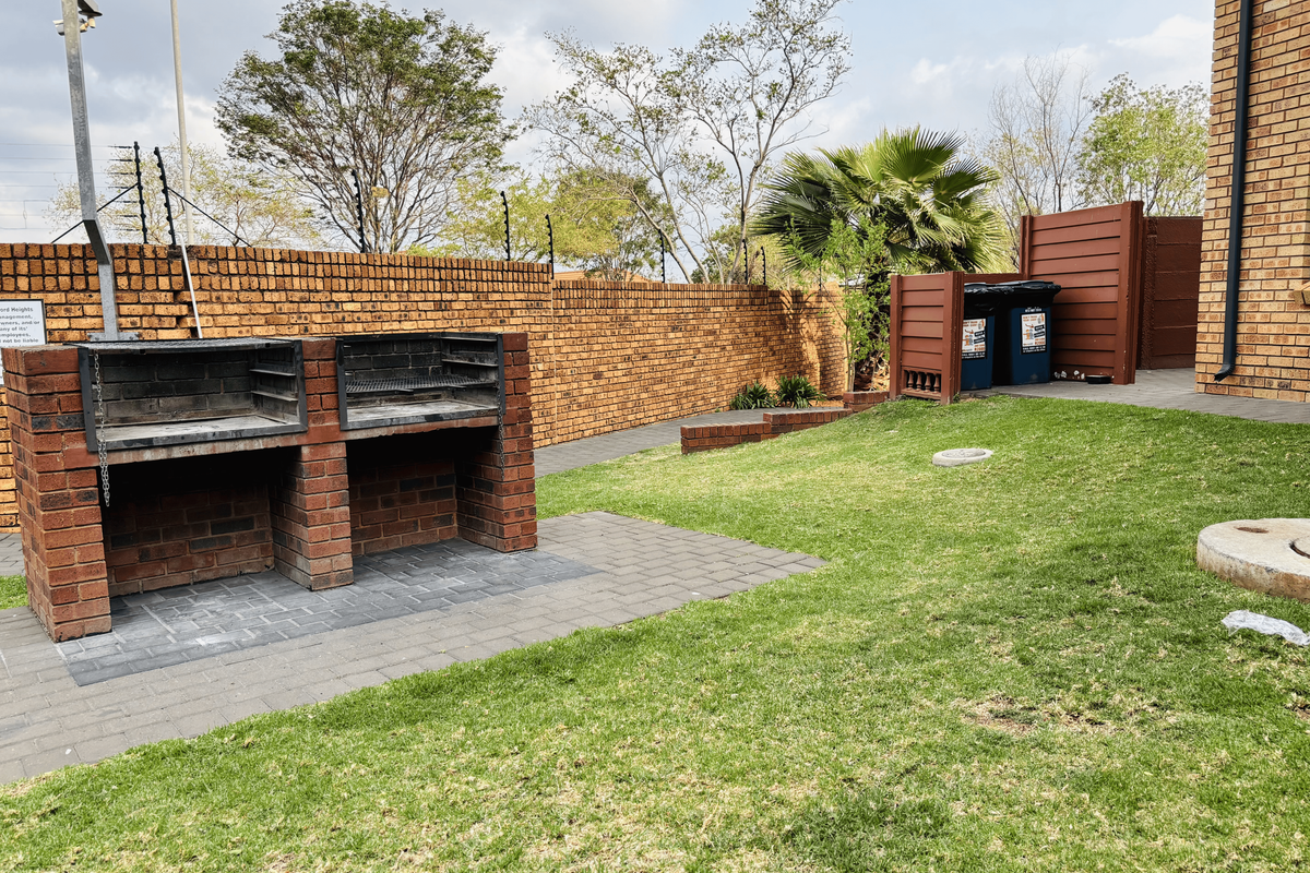 A private rear garden featuring a built-in brick braai, paved patio area, and established lawn enclosed by a brick boundary wall with electric fencing.