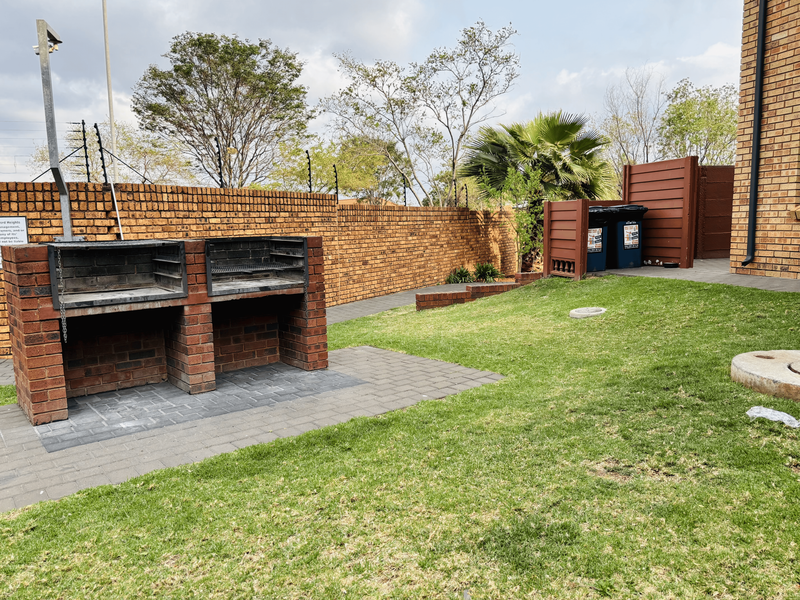 A private rear garden featuring a built-in brick braai, paved patio area, and established lawn enclosed by a brick boundary wall with electric fencing.