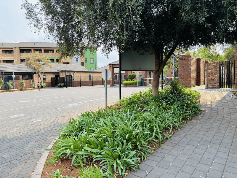 Exterior view of the apartment complex entrance featuring a paved driveway, brick boundary walls, and established garden landscaping.
