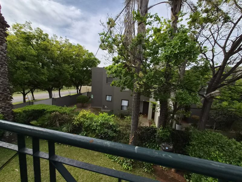 Elevated view from a balcony overlooking a lush garden area and the townhouse complex exterior.