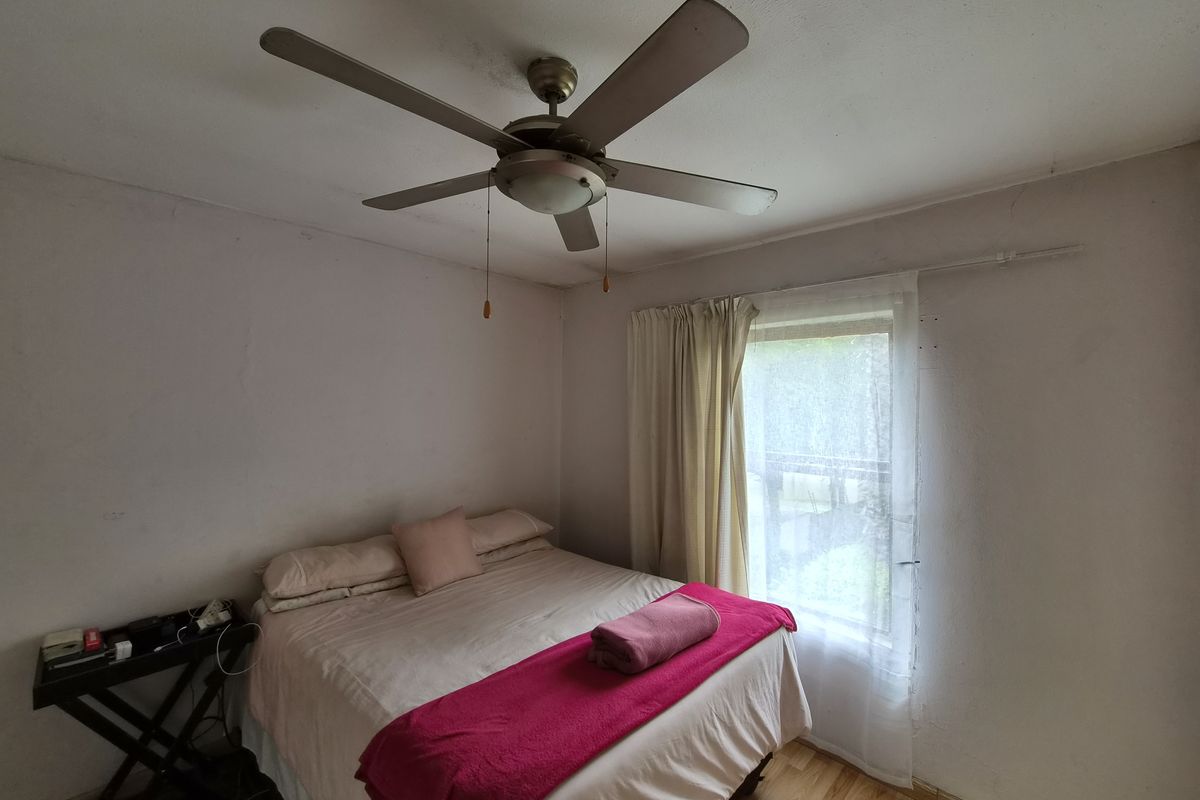 A bedroom featuring laminate flooring, a ceiling fan, and a window. The walls show signs of wear and require maintenance.
