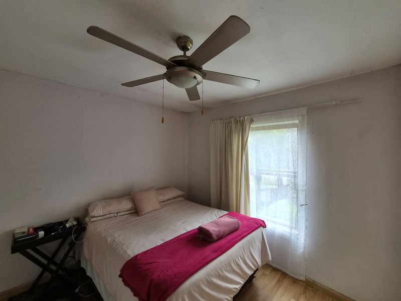 A bedroom featuring laminate flooring, a ceiling fan, and a window. The walls show signs of wear and require maintenance.