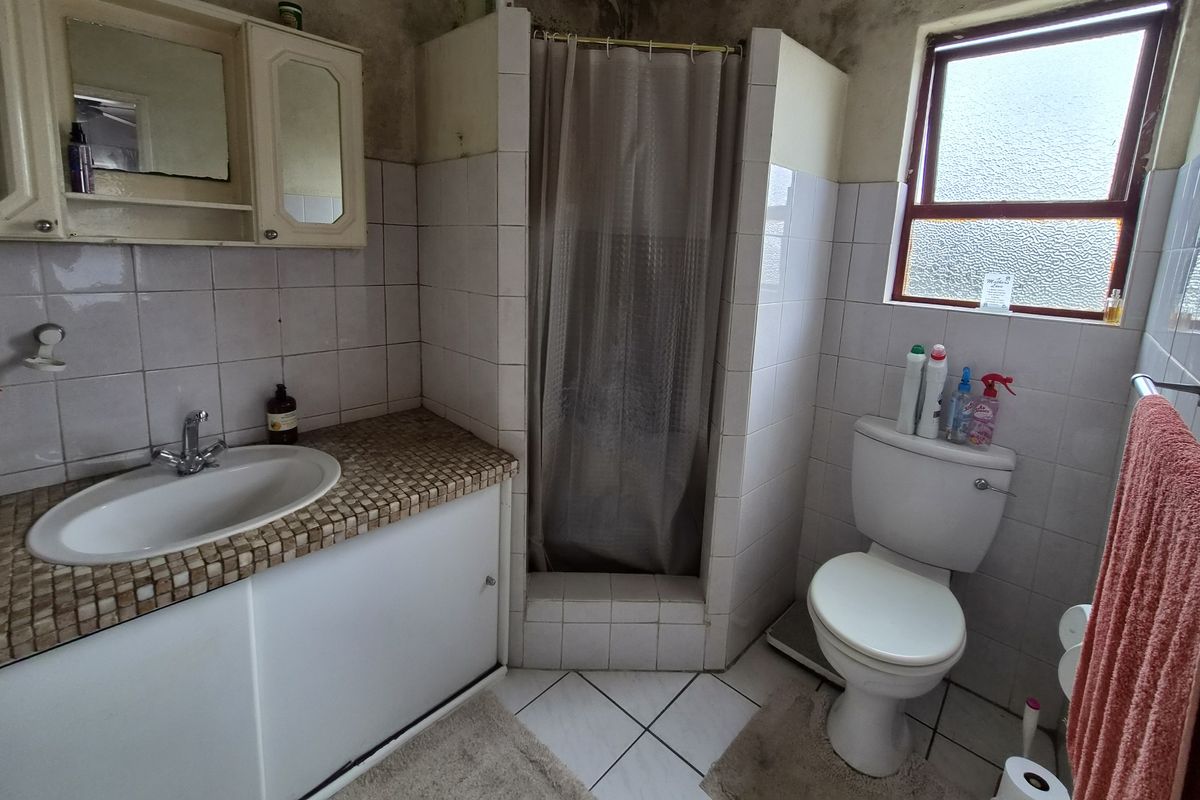 A dated bathroom featuring a vanity, shower enclosure, and toilet, currently showing significant signs of wall and ceiling deterioration requiring maintenance.