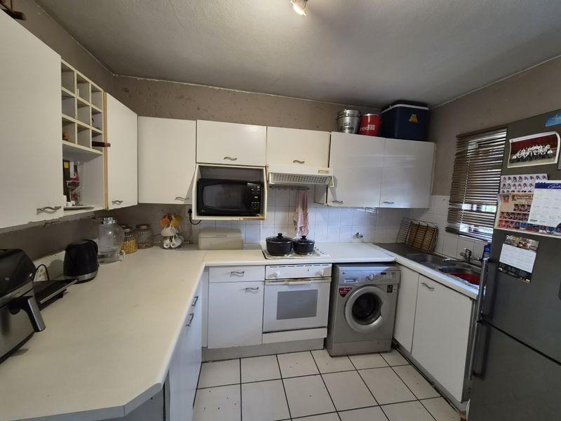 Functional kitchen featuring white cabinetry, laminate countertops, built-in oven with extractor, and tiled flooring. The space would benefit from cosmetic updates and fresh paint.