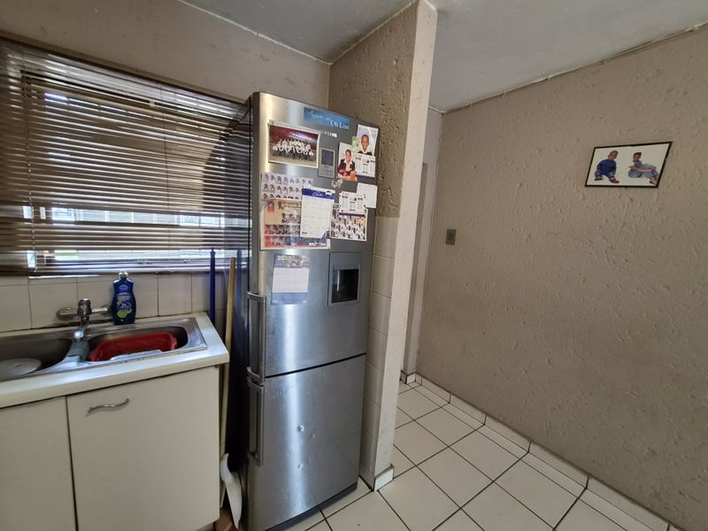 A compact kitchen area featuring a stainless steel sink, tiled flooring, and textured walls, offering a functional space with potential for modern updates.