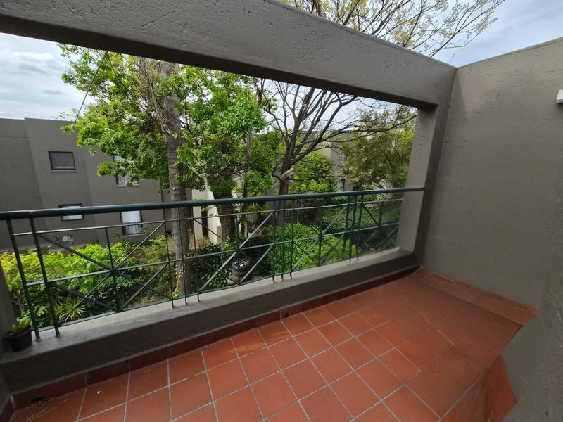 A covered balcony featuring terracotta tiling and a metal balustrade, offering an elevated view of the surrounding complex greenery.
