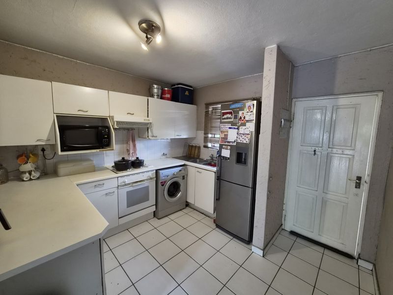 A functional kitchen featuring white cabinetry, laminate countertops, built-in oven, and tiled flooring, offering a practical layout with direct access to the exterior.
