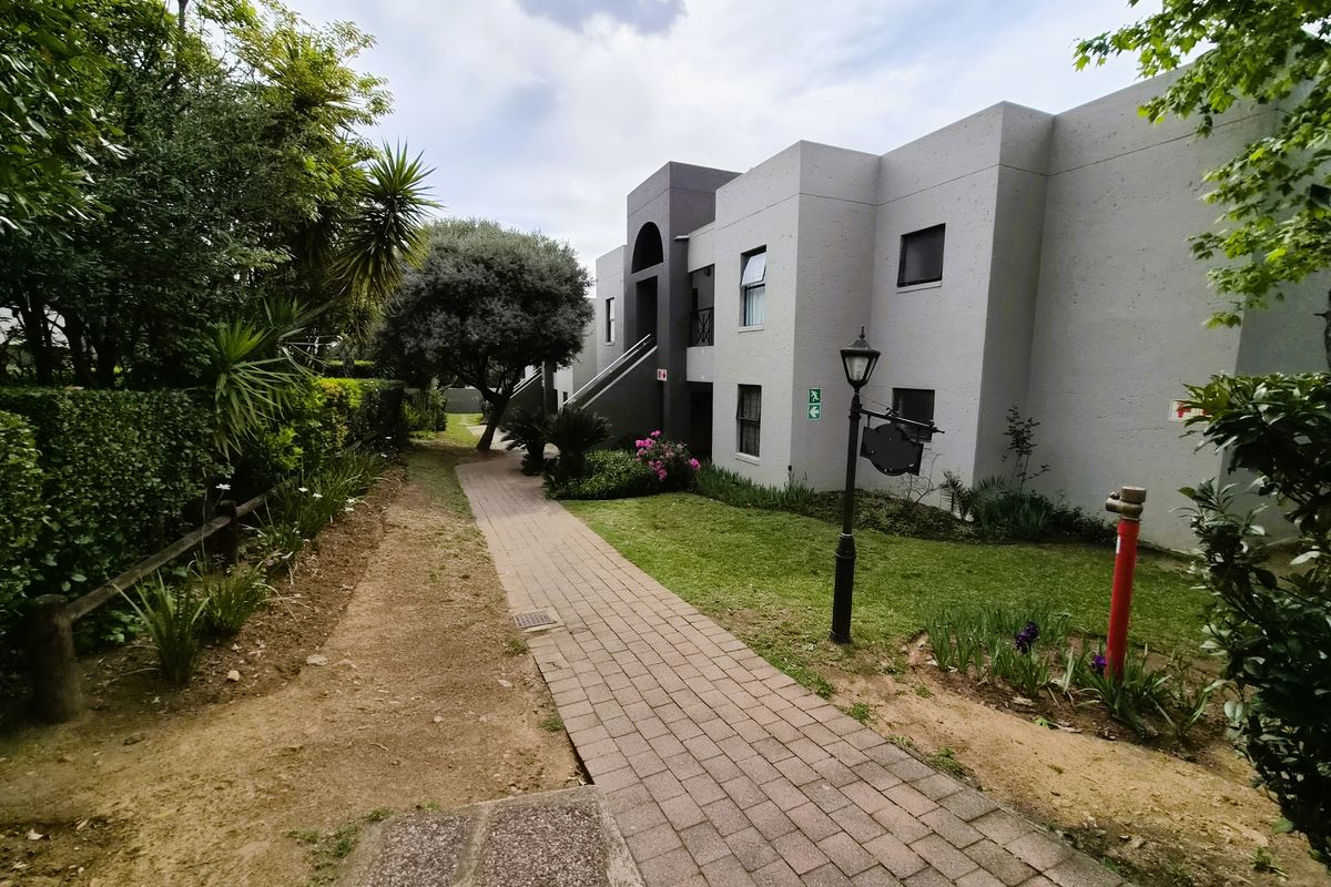 A well-maintained exterior view of the townhouse complex featuring a paved walkway, landscaped garden areas, and exterior building access.