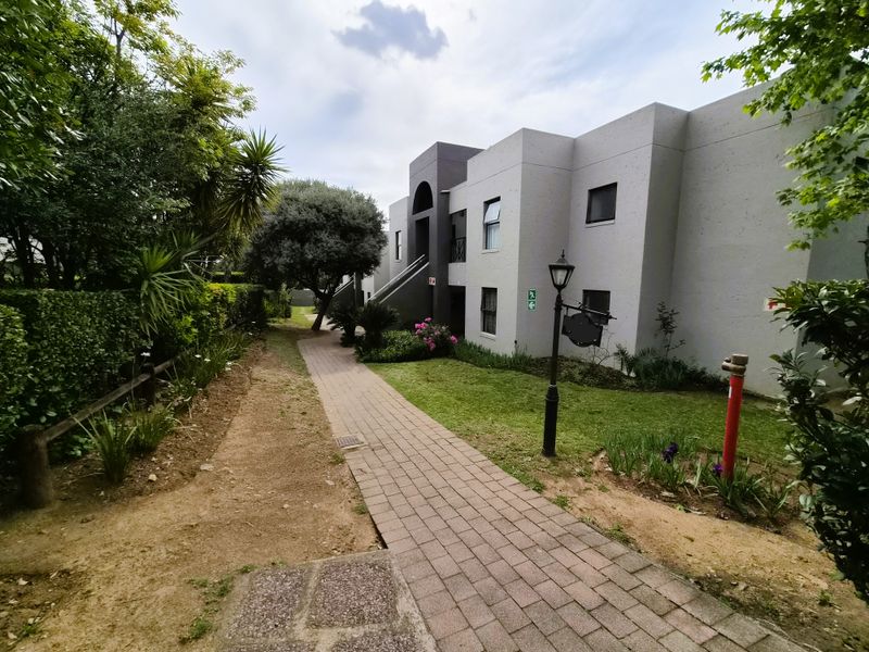A well-maintained exterior view of the townhouse complex featuring a paved walkway, landscaped garden areas, and exterior building access.