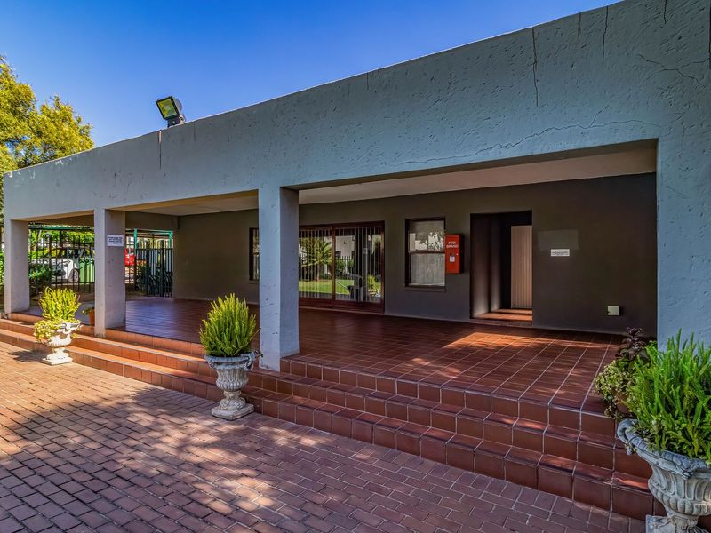 A spacious covered patio area featuring tiled flooring, concrete support pillars, and a fire hose reel, providing a functional outdoor entertainment space.