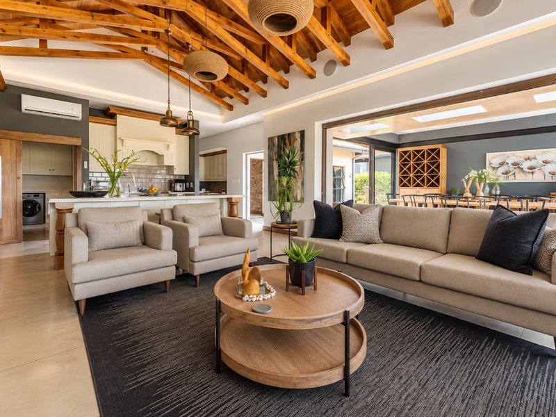 Spacious open-plan living area featuring exposed timber trusses, modern kitchen with subway tile backsplash, and seamless flow to the outdoor patio through large sliding doors.