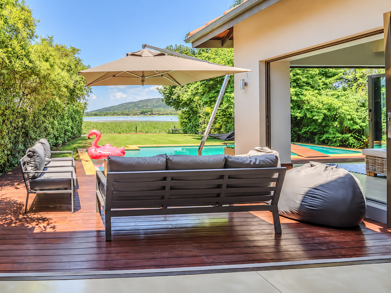A spacious covered timber deck featuring seamless indoor-outdoor flow through stacking glass doors, overlooking a private swimming pool and scenic lake views.