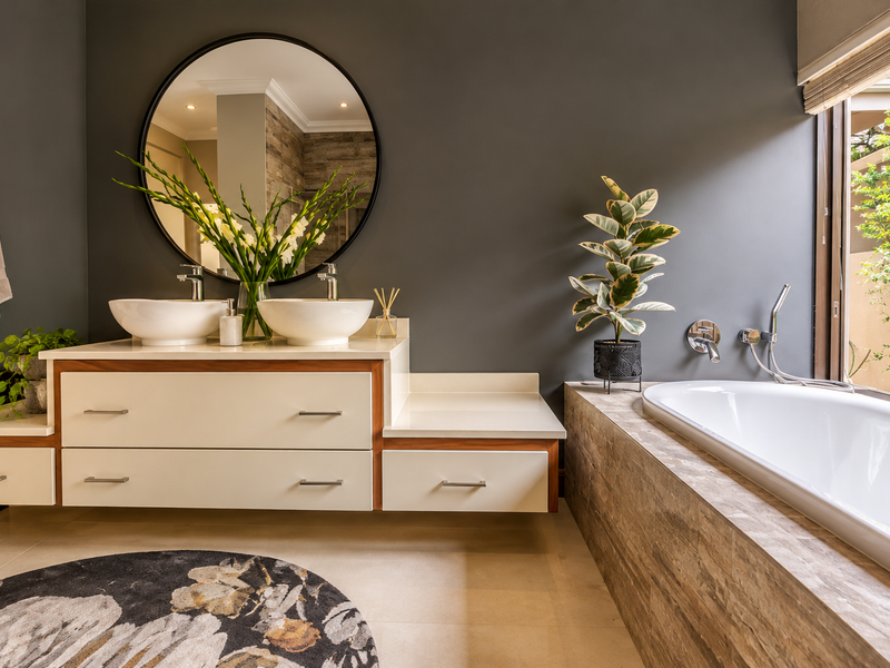 Modern bathroom featuring a double vanity with vessel sinks, a built-in bathtub with stone tile surround, and a large round mirror.