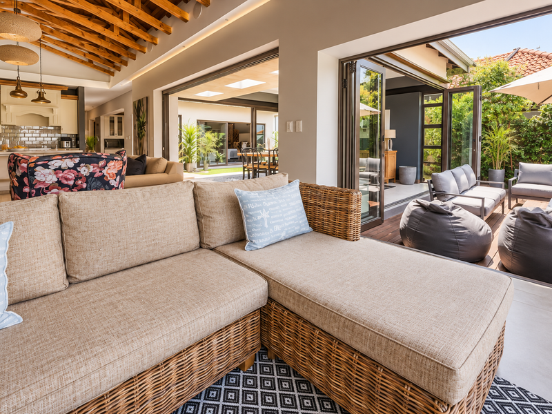 Spacious open-plan living area featuring exposed timber beams, modern kitchen, and seamless indoor-outdoor flow through large bi-fold doors to a timber deck.