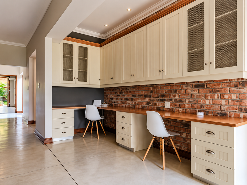 A well-appointed home office featuring custom built-in cabinetry, a spacious wooden desk, exposed brick wall accents, and polished concrete flooring.