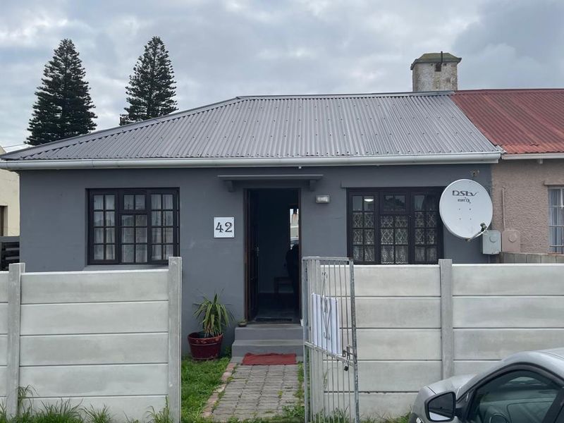 Front elevation of a townhouse featuring a grey facade, corrugated metal roof, and a precast concrete boundary wall with a gated entrance.