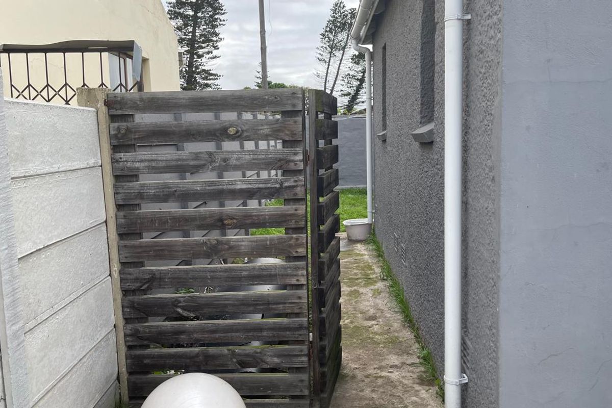 A narrow side passage of the townhouse featuring a concrete pathway, a timber privacy screen, and exterior wall with a downpipe.