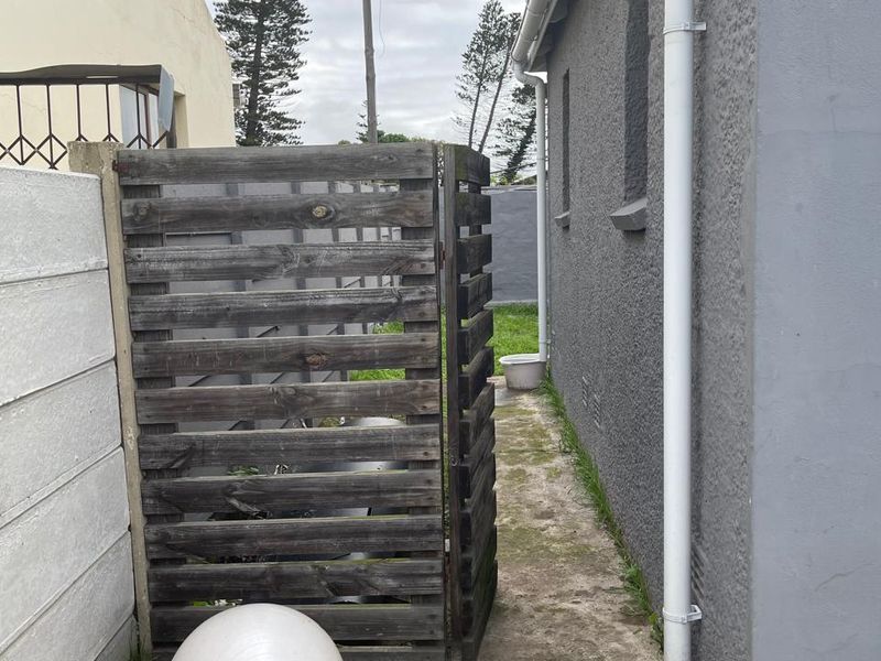 A narrow side passage of the townhouse featuring a concrete pathway, a timber privacy screen, and exterior wall with a downpipe.