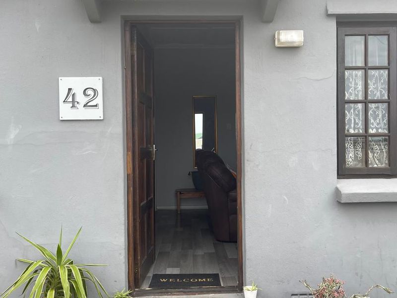 Front entrance of a townhouse featuring a timber door, house number plaque, and grey exterior walls with visible plaster cracking.